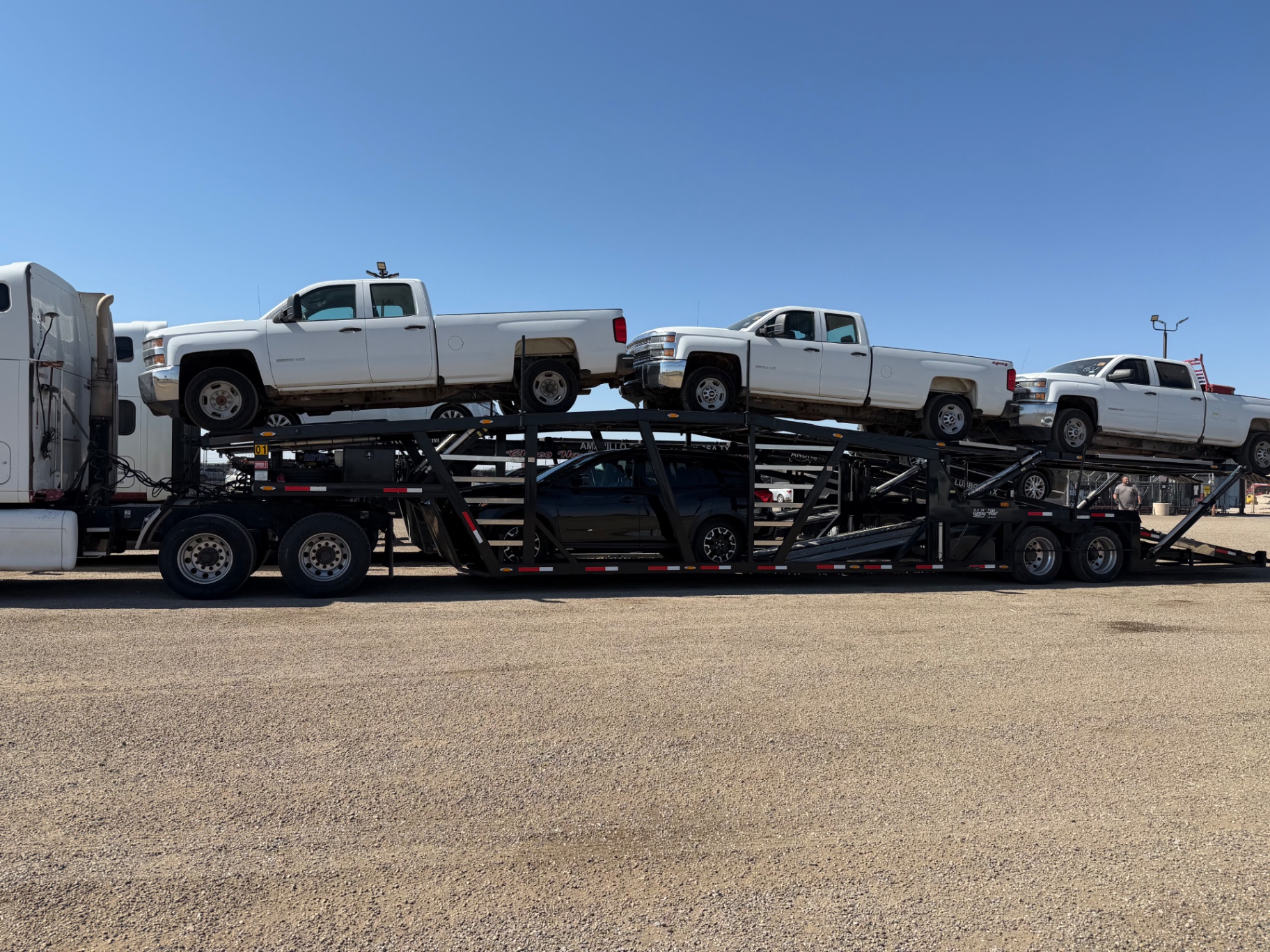 Multi-level car hauler loaded with white pickup trucks and other vehicles