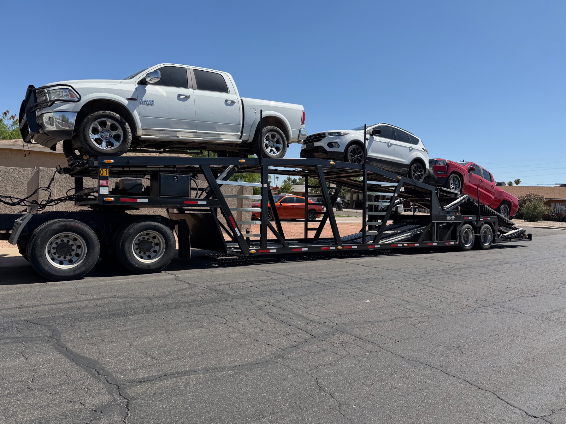 White Ram pickup, white SUV and red pickup on a car hauler