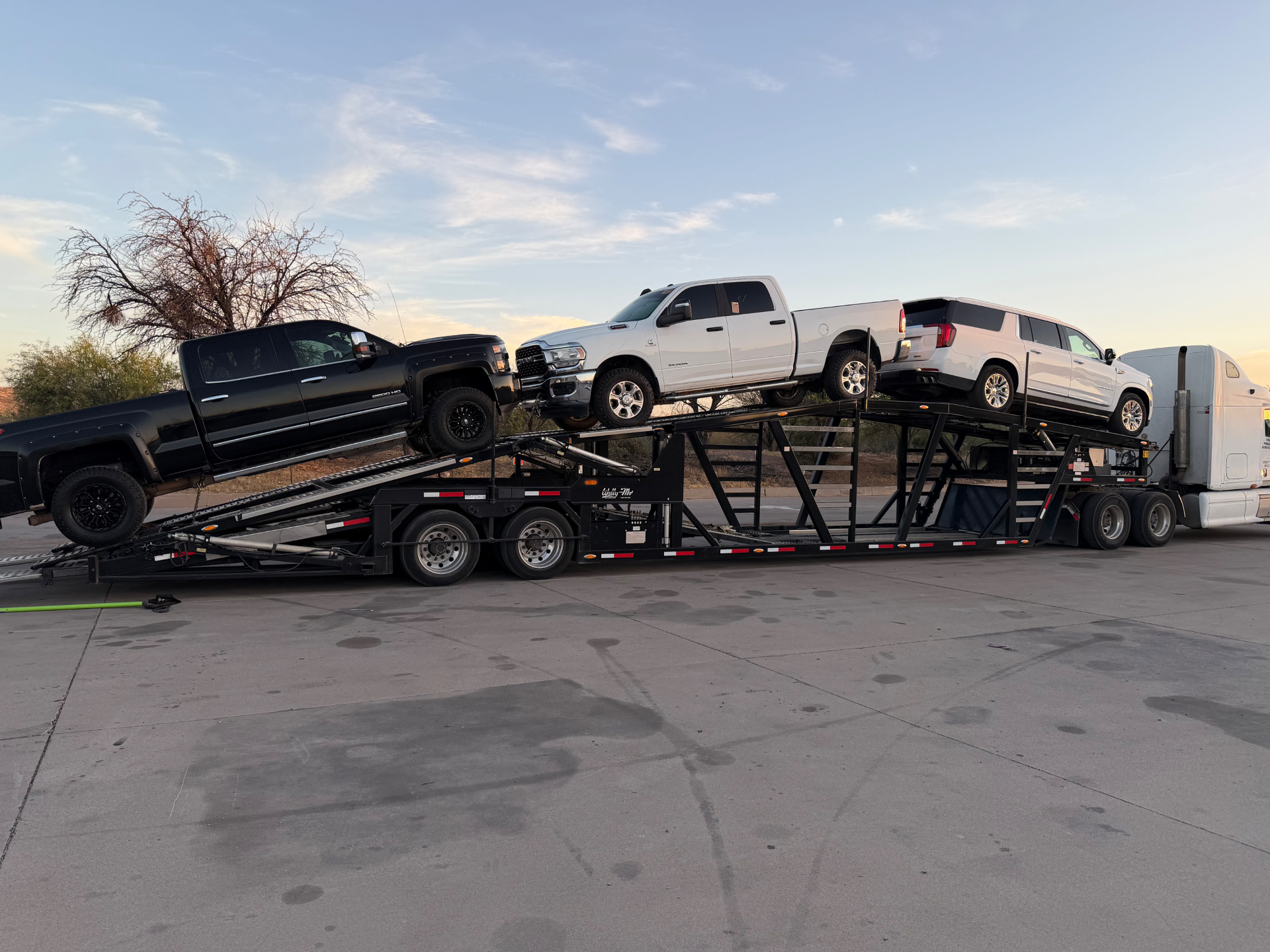 Black pickup, white pickup and white SUV secured on a car-hauling trailer